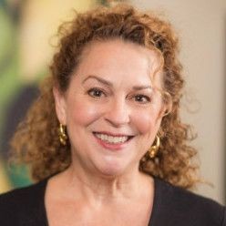 Smiling woman with curly hair wearing gold hoop earrings and a black top.