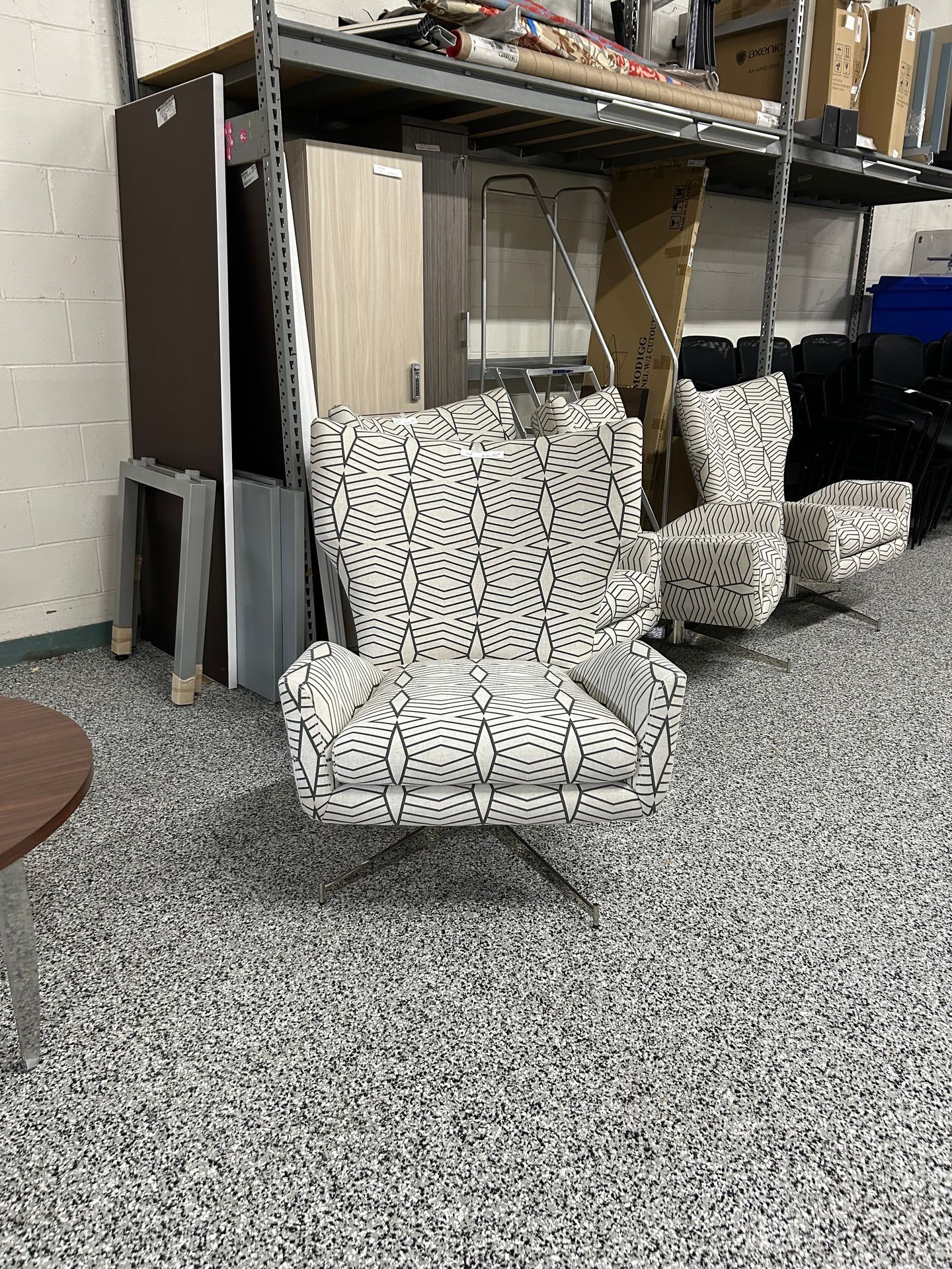 Patterned chair on speckled floor in a storage room with shelves and stacked items.